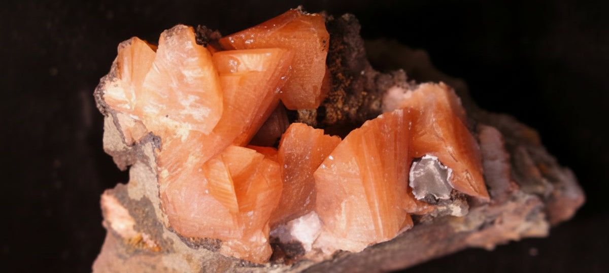 A Heulandite mineral specimen featuring bright orange-pink crystal clusters on a rough, earthy brown matrix, set against a solid black background.